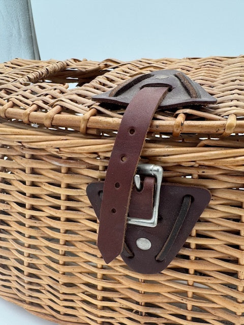 Orvis wicker basket close-up showing leather strap and woven design, ideal for outdoor adventures and organizing gear.